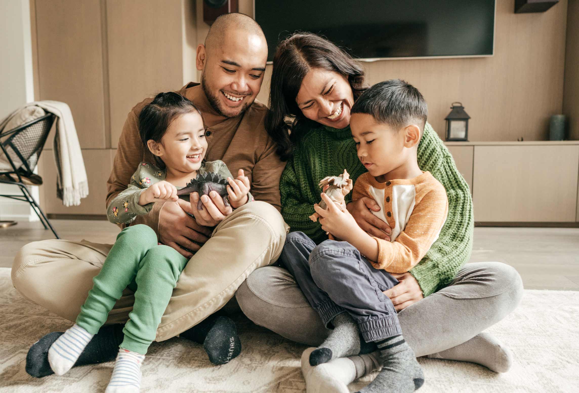 Young family man, woman, boy and girl sitting on floor of living room . They are happy and smiling.