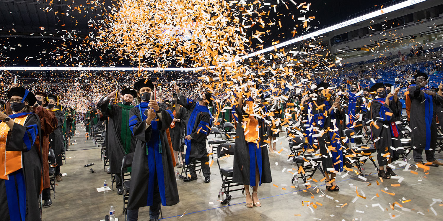 Students graduating in a stadium and throwing orange and white confetti.